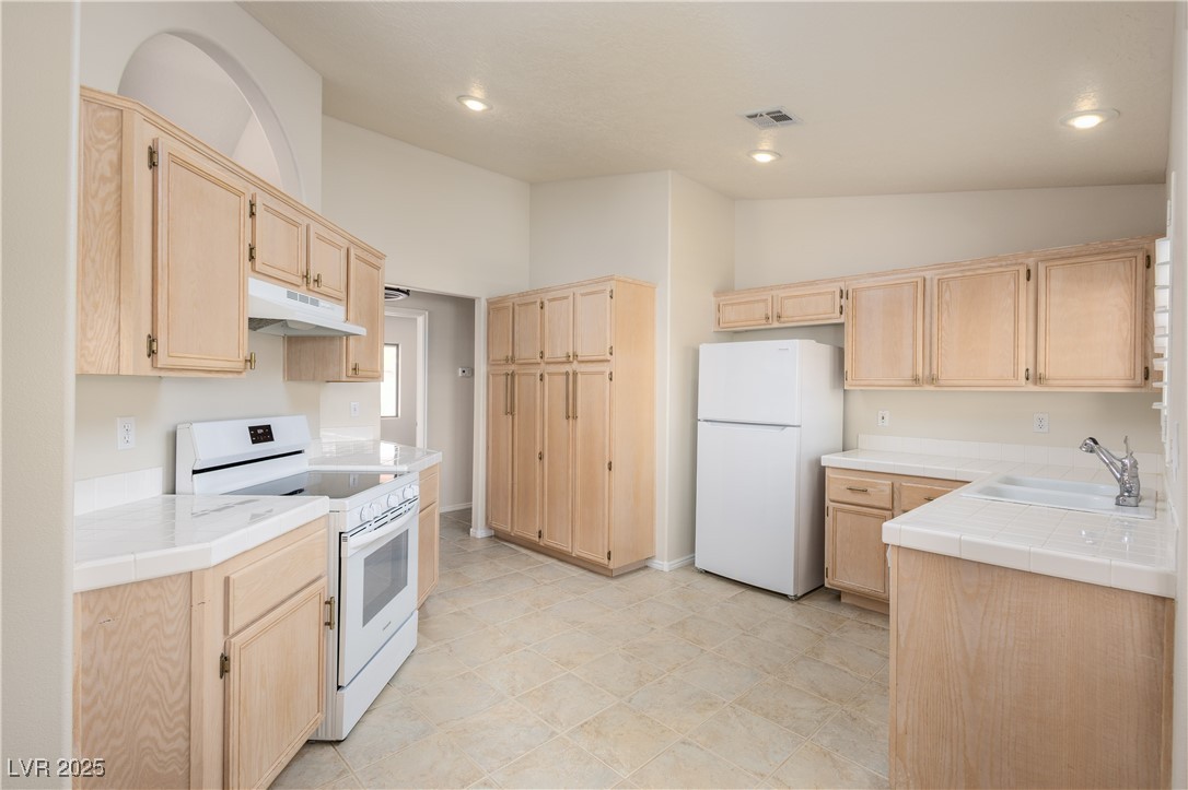 490 Ruby Drive Mesquite, NV 89027 - Photo 2 of 23 Kitchen with light brown cabinetry, tile counters, white appliances, recessed lighting, and lofted ceiling