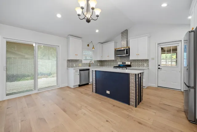 a kitchen with stainless steel appliances granite countertop a stove top oven a sink dishwasher a refrigerator and white cabinets with wooden floor