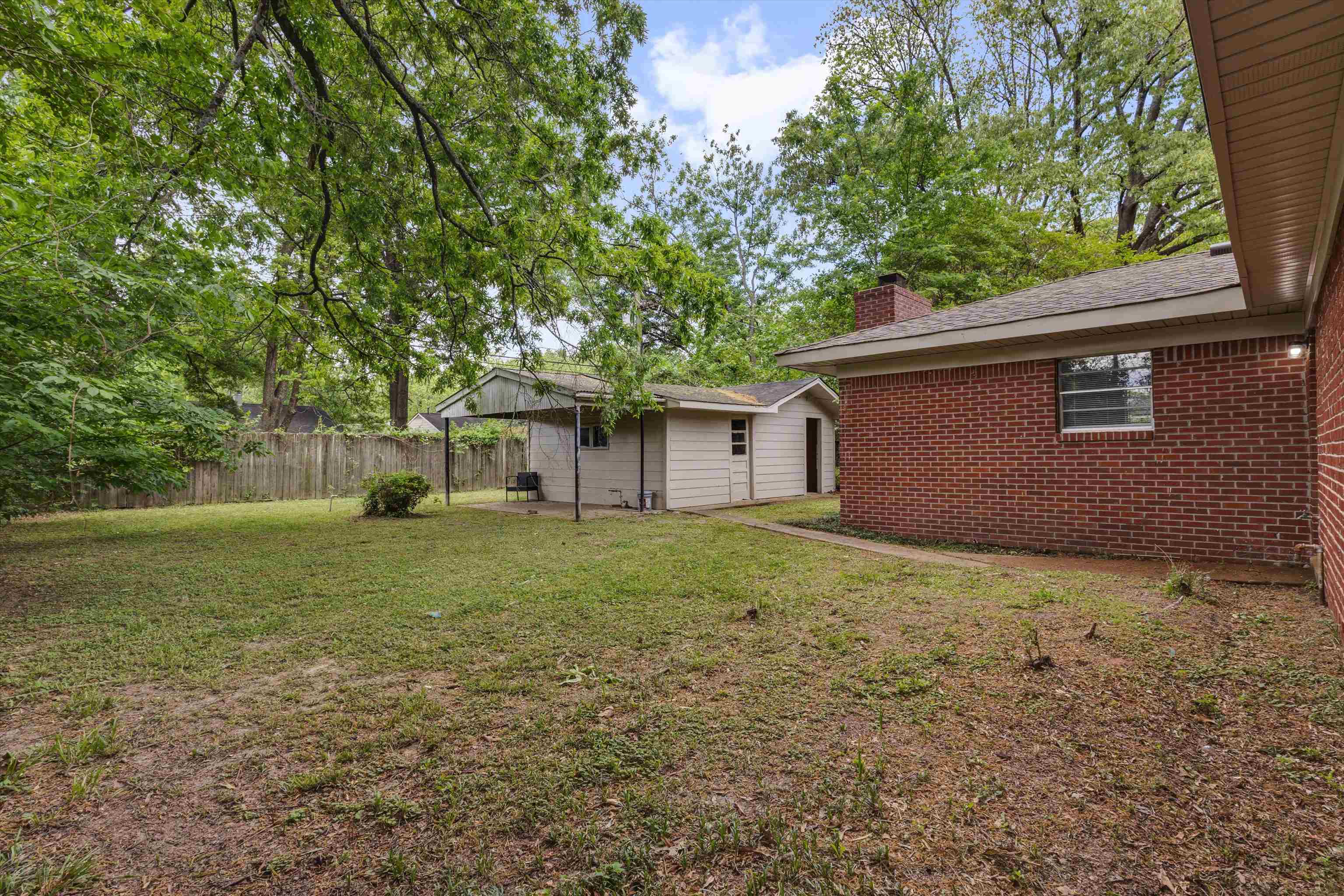 4565 Verne Road Memphis, TN 38117 - Photo 16 of 18 Expansive backyard featuring a brick exterior structure, a separate outbuilding with a covered patio area, and mature trees providing natural canopy