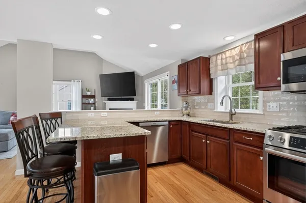 a kitchen with stainless steel appliances granite countertop a stove top oven a sink dishwasher a dining table and chairs with wooden floor