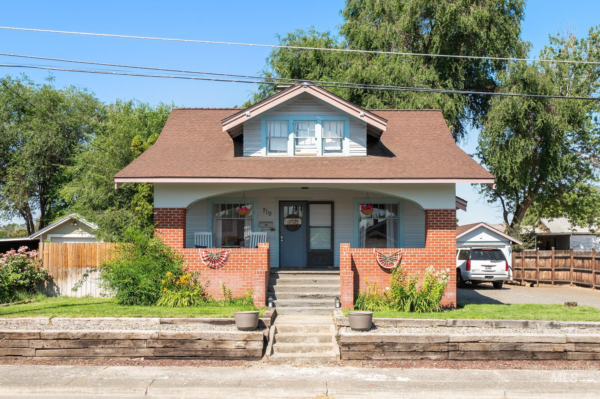 Bungalow featuring brick siding, covered porch, roof with shingles, and driveway