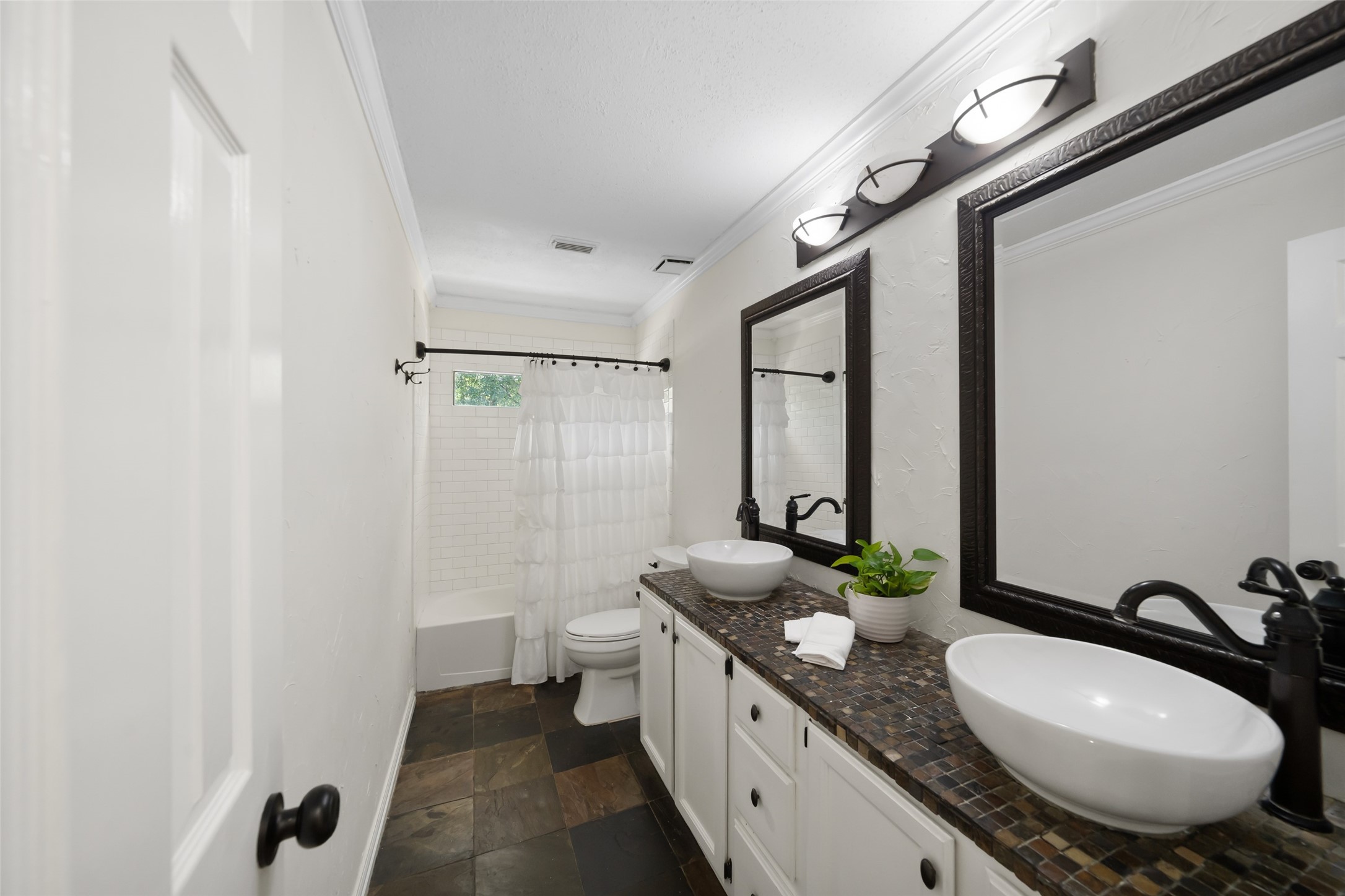 3 East Stony Bridge Circle Spring, TX 77381 - Photo 34 of 42 Located on the upper level to serve the three secondary bedrooms, this bathroom features a double vanity with vessel sinks, framed mirrors, and a shower-tub combination with a tiled surround. A window provides natural light, complemented by slate flooring and a neutral color palette.