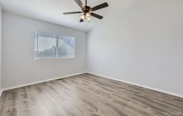an empty room with wooden floor fan and windows