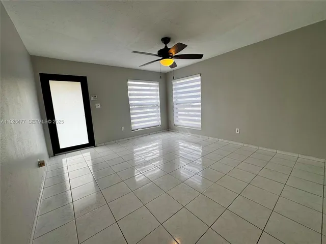 a view of an empty room with chandelier fan and window