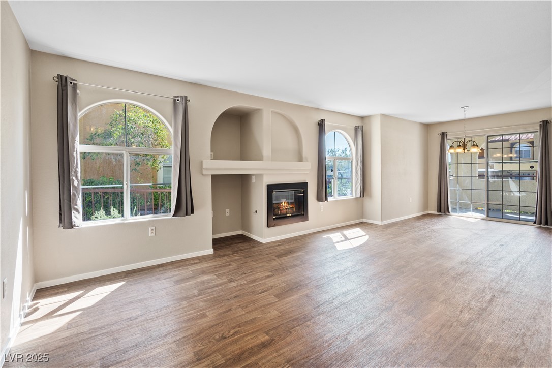 Unfurnished living room featuring a glass covered fireplace, wood finished floors, and a chandelier