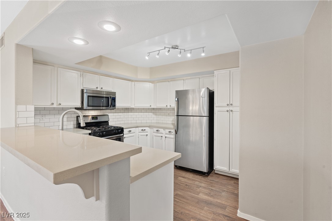 7950 West Flamingo Road, Unit 1039 Las Vegas, NV 89147 - Photo 10 of 26 Kitchen with stainless steel appliances, backsplash, a tray ceiling, a peninsula, and white cabinetry
