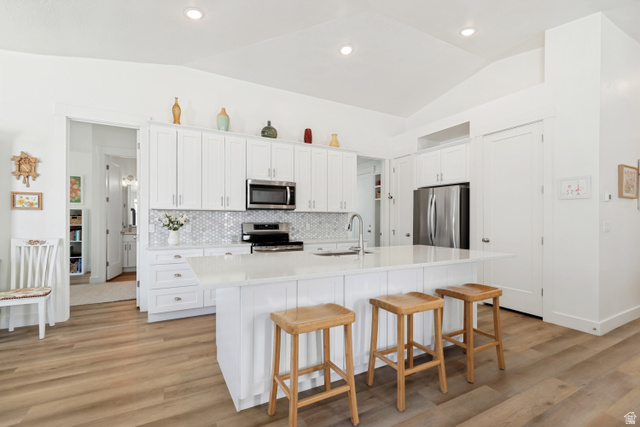 683 Kings Landing Tooele, UT 84074 - Photo 6 of 39 Kitchen featuring vaulted ceilings, wood-finish flooring, white cabinetry, a central island with countertop seating, and stainless steel appliances