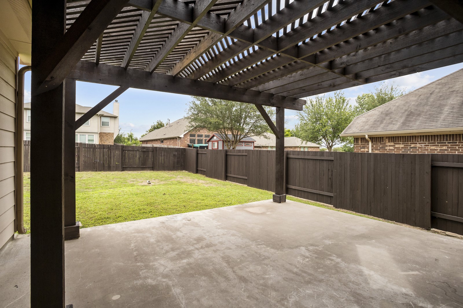 245 Razzmatazz Trail Buda, TX 78610 - Photo 33 of 37 Expansive concrete patio with a dark wood pergola, overlooking a grassy backyard with a tall wood privacy fence
