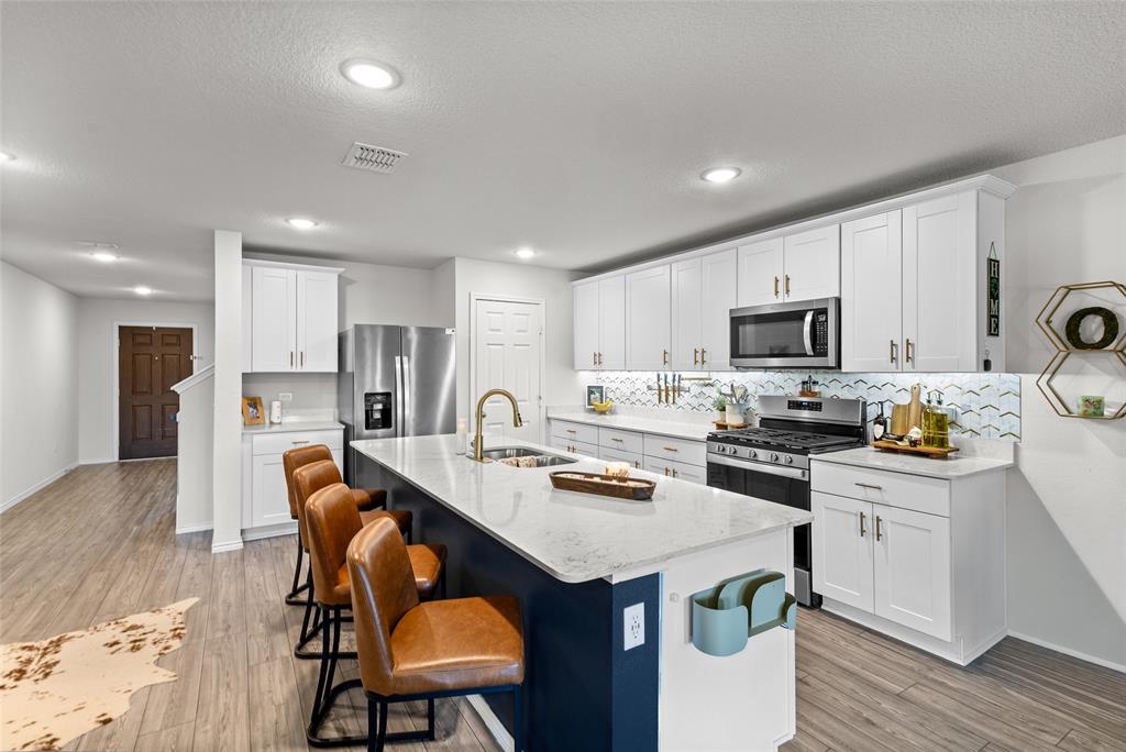 6609 Auburn Dl Road Pilot Point, TX 76258 - Photo 6 of 38 Kitchen featuring white cabinetry, stainless steel appliances, a large island with counter seating, wood-finish flooring, and recessed lighting
