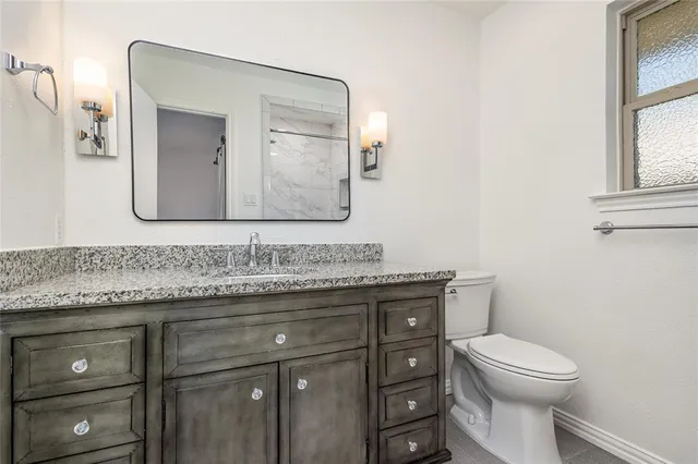 a bathroom with a granite countertop toilet sink and mirror