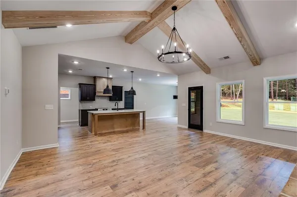 a view of an empty room and kitchen with wooden floor