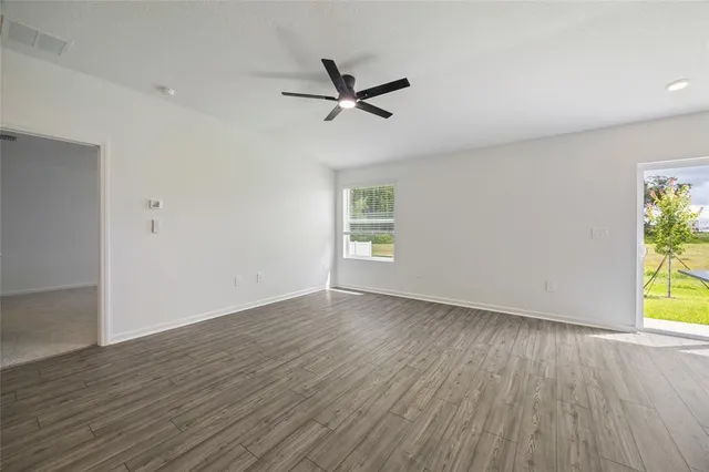 an empty room with wooden floor a ceiling fan and windows