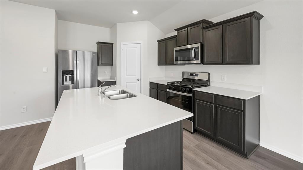1913 Freeman Street Tyler, TX 75704 - Photo 3 of 21 Kitchen with stainless steel appliances, light wood-style flooring, a kitchen island with sink, light stone counters, and vaulted ceiling