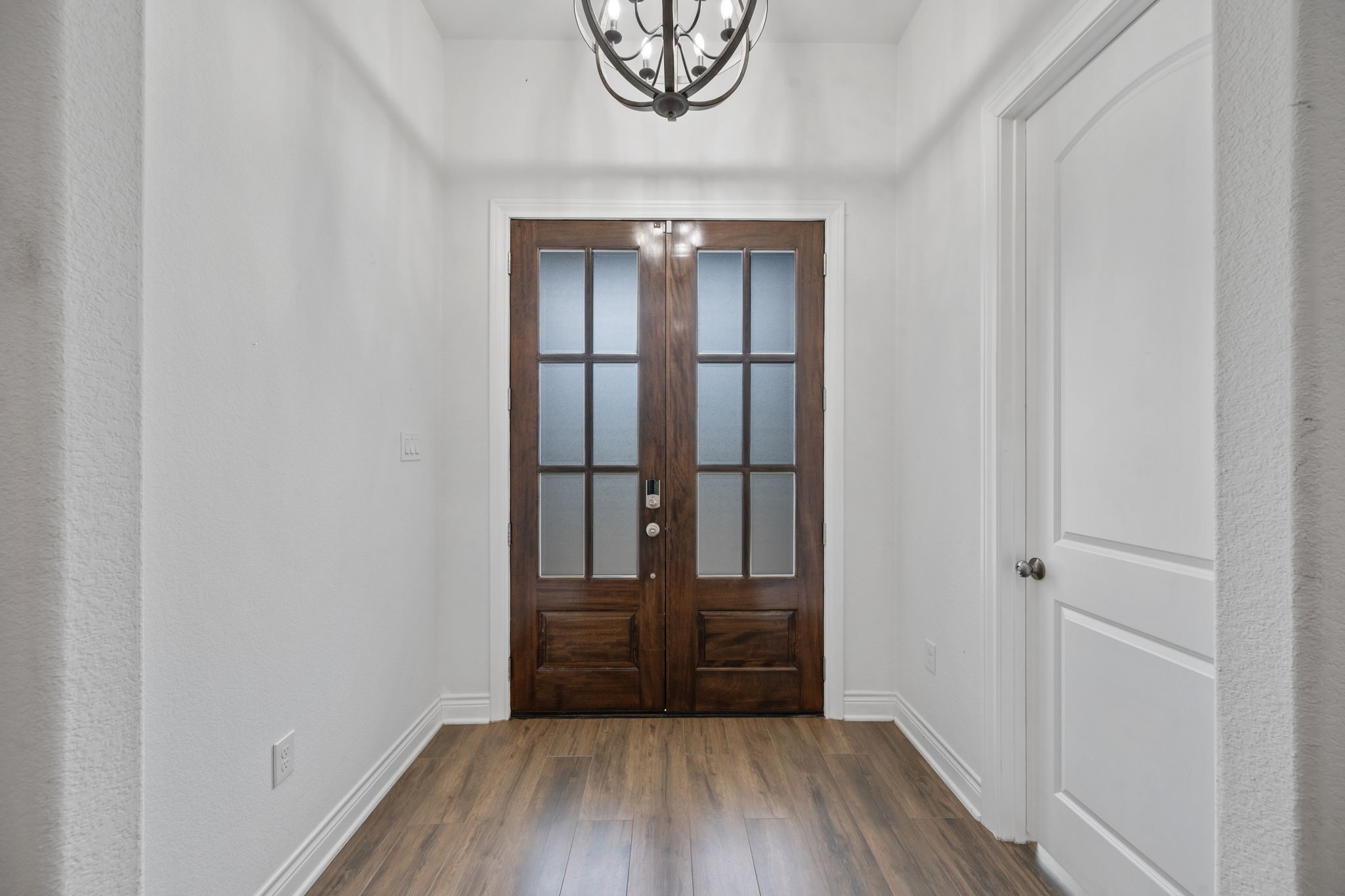 7815 Timber Switch Road Cleveland, TX 77328 - Photo 9 of 39 Elegant entranceway featuring beautiful hardwood floors, a stylish chandelier, and a striking dark wood double door with glass panels, creating a welcoming and sophisticated first impression.