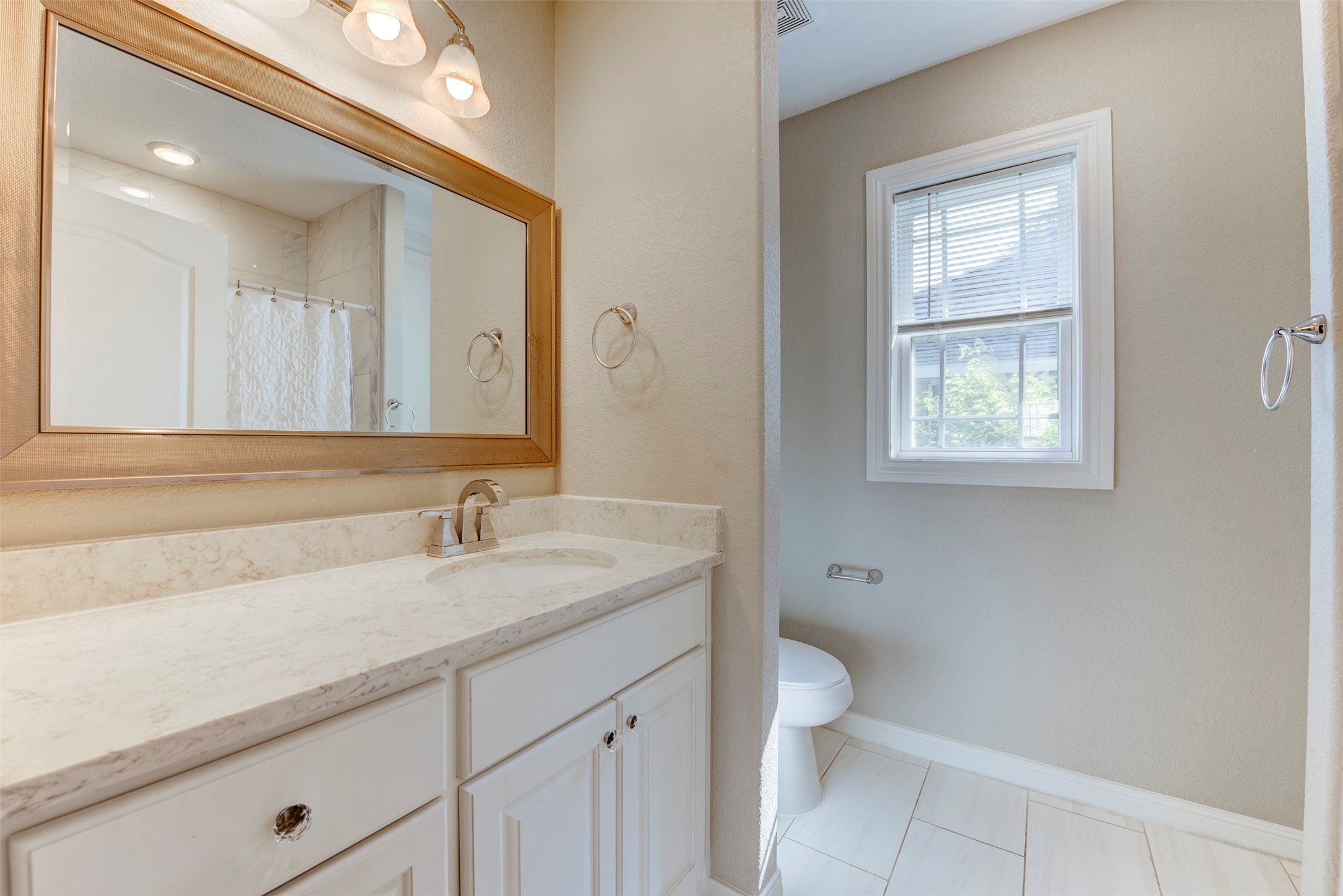 109 Dresden Street Houston, TX 77012 - Photo 33 of 43 This bathroom features a sleek, modern design with a marble countertop, under-mount sink, and a large framed mirror. It is well-lit with stylish lighting fixtures and has a window for natural light, adding to its bright and airy feel.
