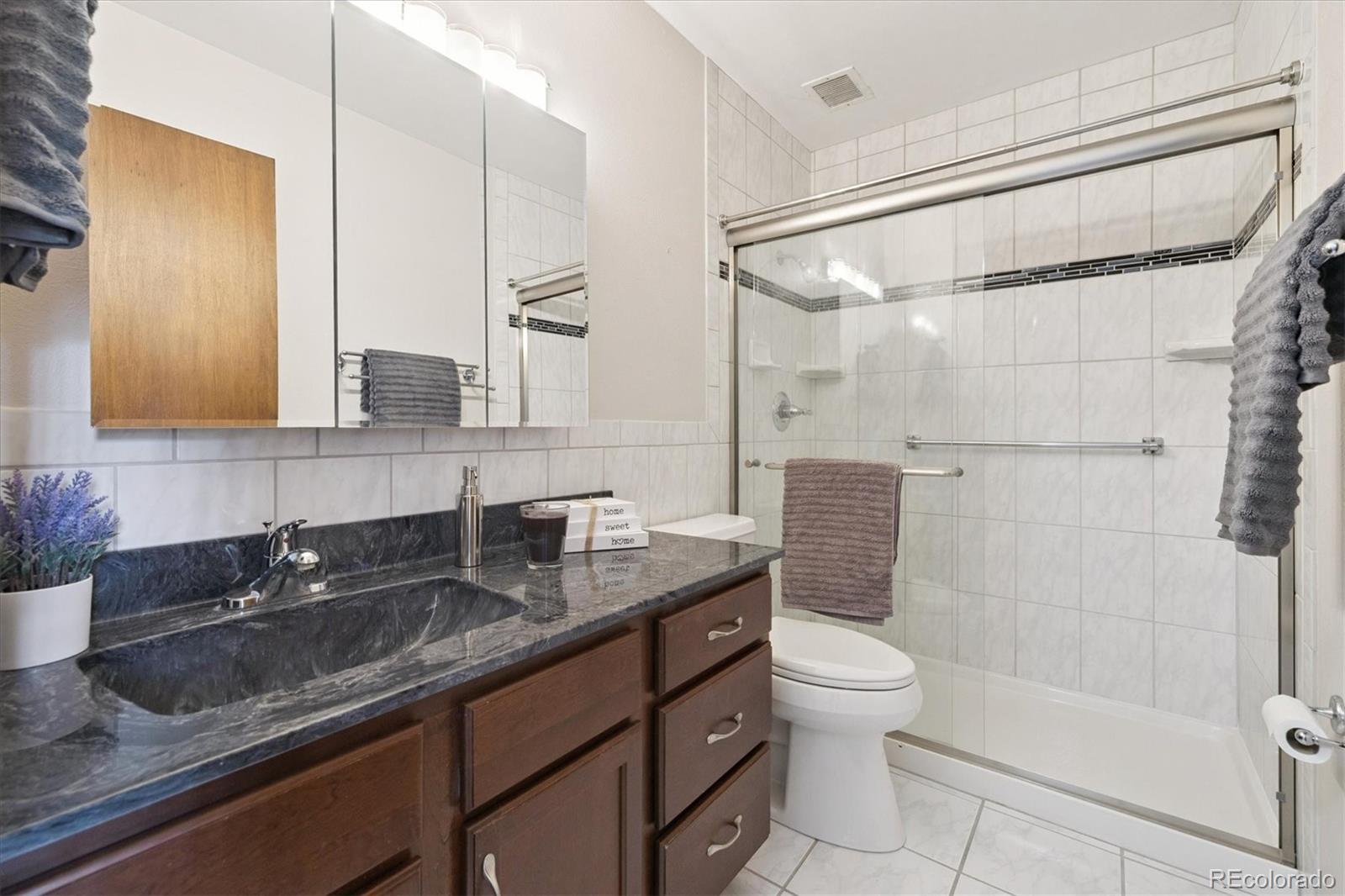 9155 Center Avenue, Unit 2D Denver, CO 80247 - Photo 12 of 50 a bathroom with a granite countertop sink a toilet and shower