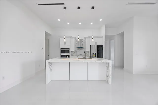 a large white kitchen with kitchen island a sink stainless steel appliances and cabinets