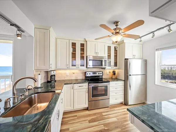 a kitchen with stainless steel appliances granite countertop a sink a stove a refrigerator cabinets a dining table and chairs