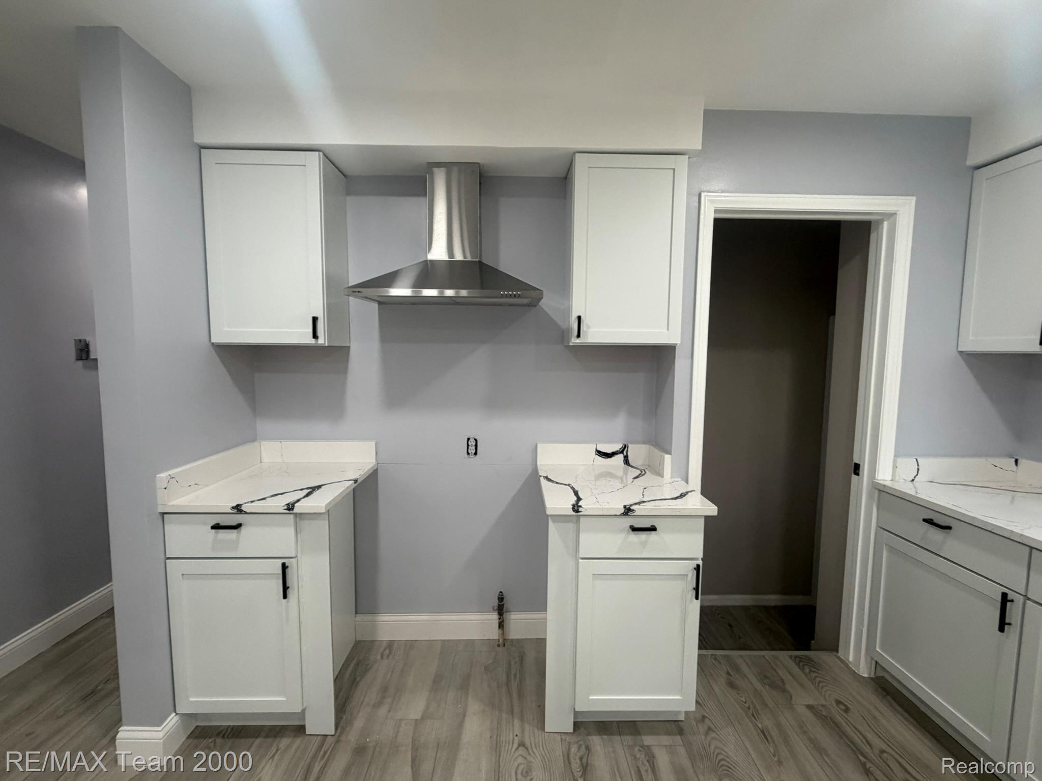 9023 Evergreen Road Detroit, MI 48228 - Photo 11 of 21 White shaker-style cabinetry with matte black hardware, quartz countertops with veining, stainless steel range hood, and wood-finish flooring