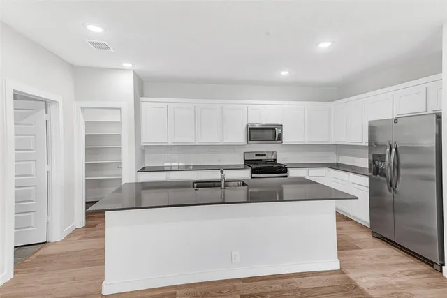 a kitchen with stainless steel appliances granite countertop a refrigerator a sink a stove a microwave and white cabinets