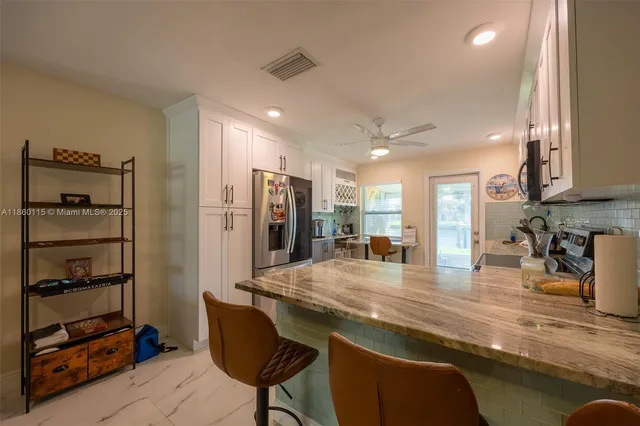 a kitchen with stainless steel appliances kitchen island granite countertop a refrigerator oven a sink dishwasher and white cabinets with wooden floor