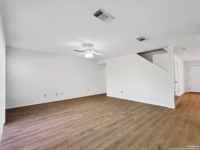a view of an empty room with wooden floor and fan