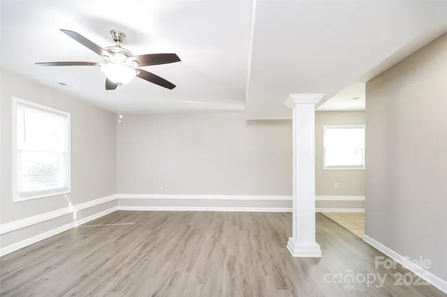 an empty room with wooden floor fan and windows