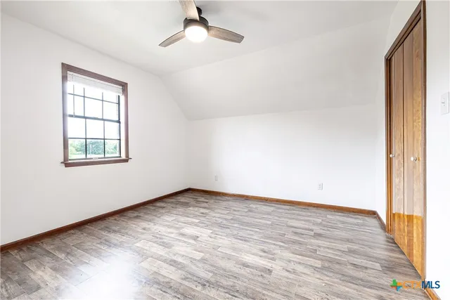 an empty room with wooden floor fan and windows