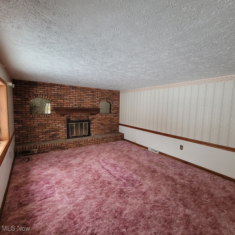38227 Chestnut Ridge Road Elyria, OH 44035 - Photo 9 of 36 Unfurnished living room featuring a brick fireplace, a textured ceiling, and dark colored carpet