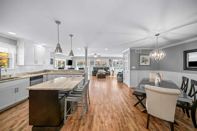 a kitchen with stainless steel appliances granite countertop a refrigerator a sink dishwasher a stove and a dining table with wooden floor