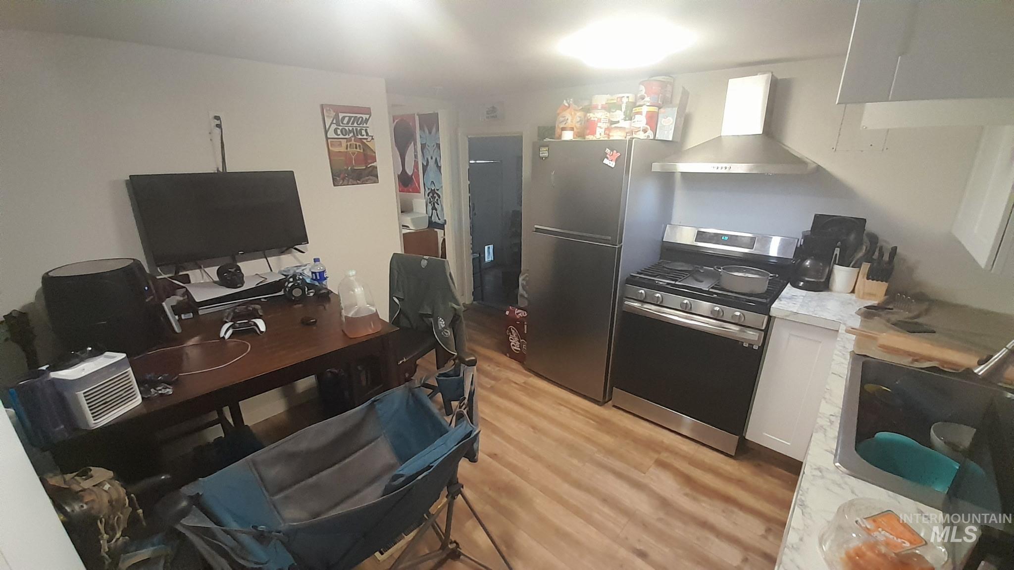 111 East Simplot Boulevard, Unit 37 Caldwell, ID 83605 - Photo 5 of 12 Kitchen featuring stainless steel range with gas stovetop, light countertops, white cabinetry, wall chimney exhaust hood, and a desk