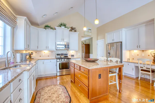 a kitchen with stainless steel appliances granite countertop a stove top oven a sink dishwasher and white cabinets with wooden floor