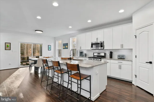 a kitchen with stainless steel appliances granite countertop a refrigerator a stove top oven a sink dishwasher a dining table and chairs with wooden floor