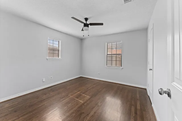 an empty room with wooden floor ceiling fan and windows