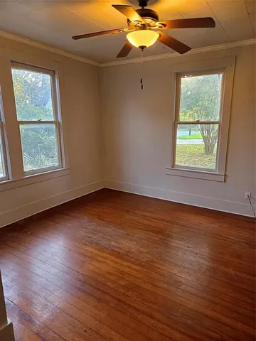 an empty room with wooden floor chandelier fan and windows