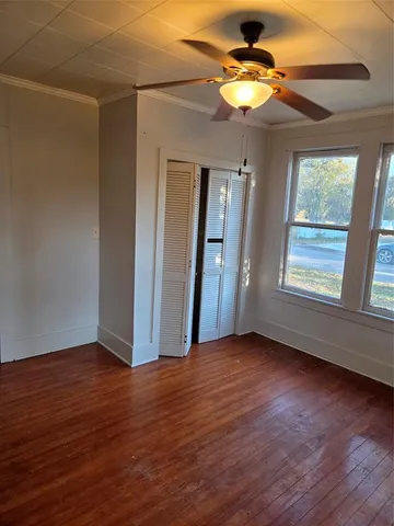 an empty room with wooden floor chandelier fan and windows