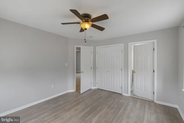 a view of an empty room with wooden floor and a ceiling fan