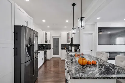 a kitchen with stainless steel appliances kitchen island granite countertop a refrigerator a stove and a sink with wooden floor