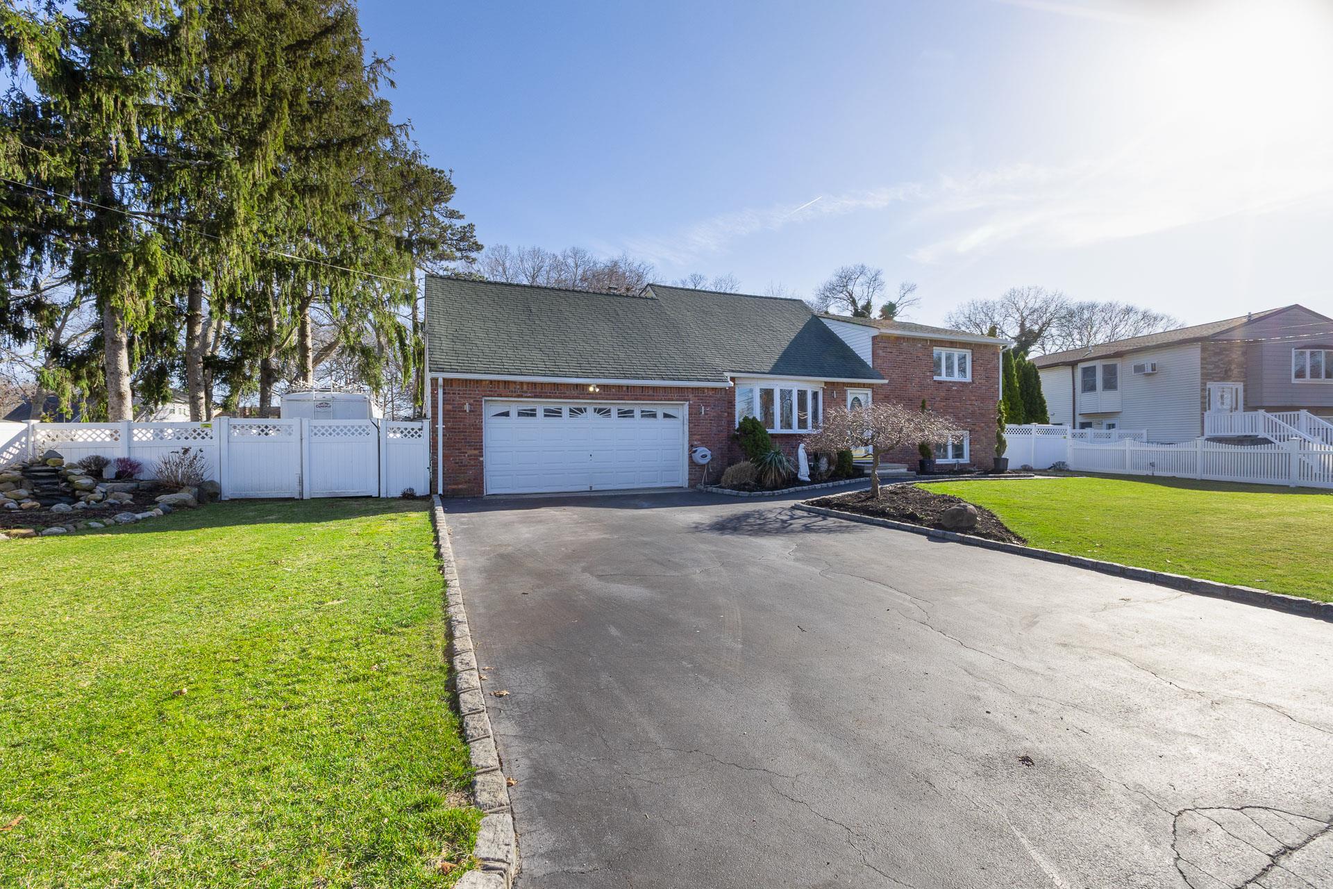 84 Riverside Avenue Mastic Beach, NY 11951 - Photo 2 of 32 View of front of house with fence, an attached garage, aphalt driveway, a front yard, and brick siding