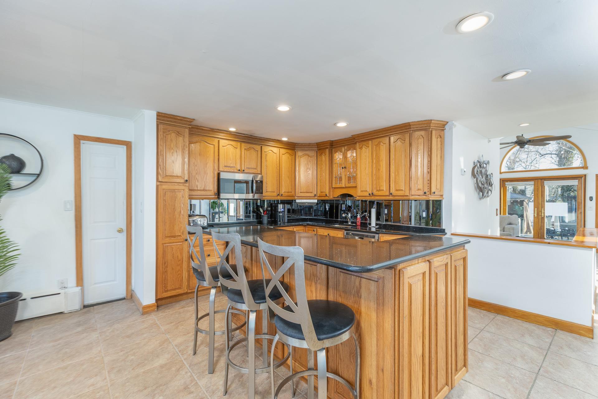 84 Riverside Avenue Mastic Beach, NY 11951 - Photo 5 of 32 Kitchen featuring a kitchen bar, brown cabinets, stainless steel microwave, dark countertops, and recessed lighting