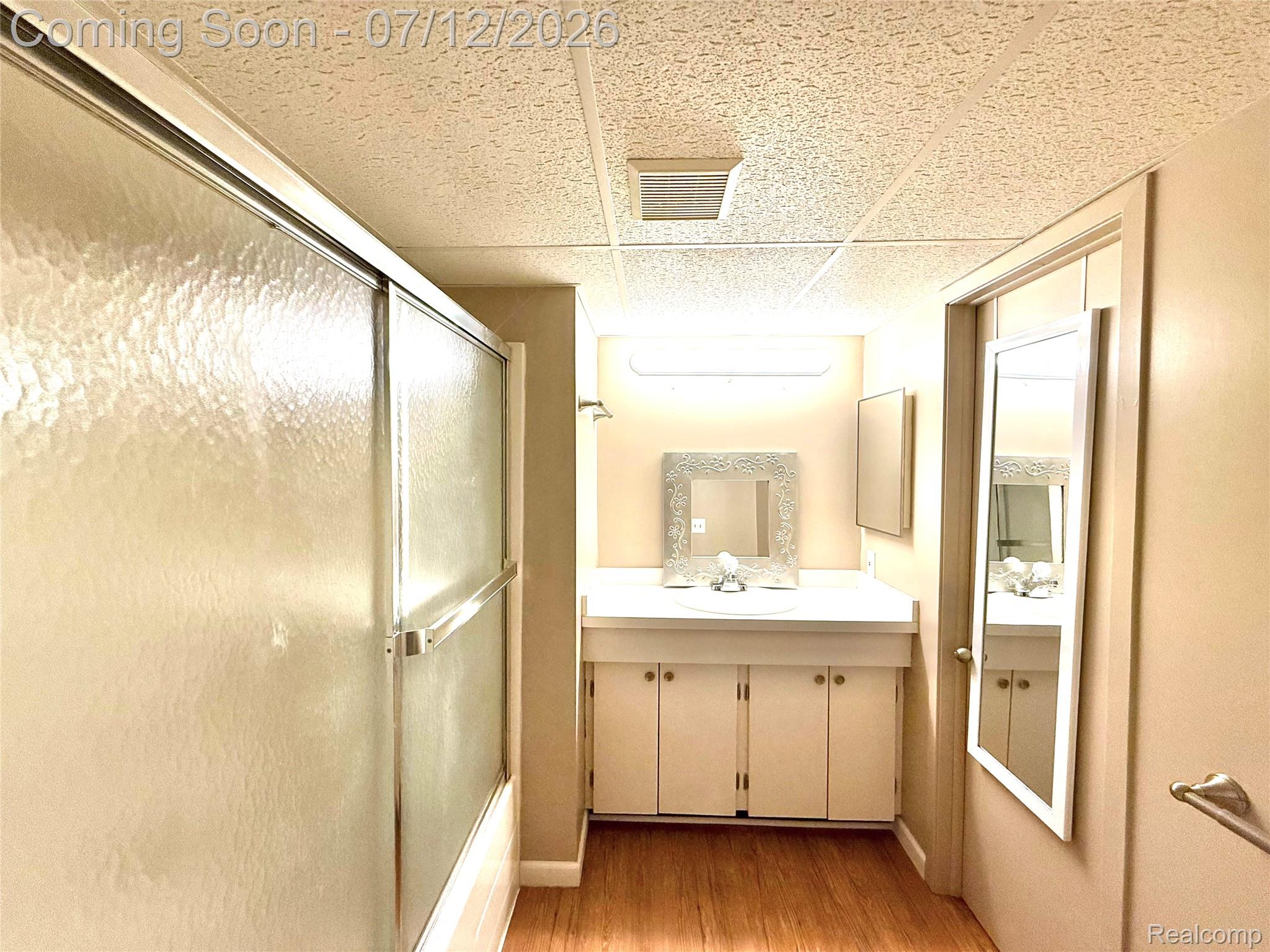 2033 Avonstoke Road Rochester, MI 48307 - Photo 18 of 26 Bathroom featuring a tub and shower combination with sliding textured glass doors, a vanity with a white countertop and integrated sink, a single-door vanity cabinet, and wood-finish flooring