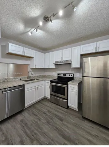 a kitchen with granite countertop a refrigerator stove top oven and cabinets