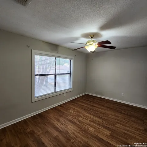 an empty room with wooden floor fan and windows