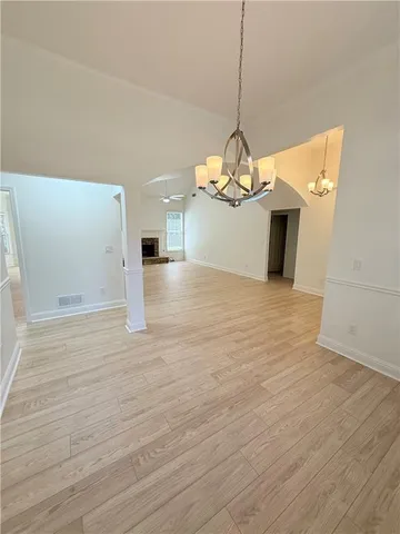 a view of a room with wooden floor a chandelier a ceiling fan and kitchen space