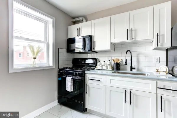 a kitchen with stainless steel appliances granite countertop white cabinets a stove a sink and a window