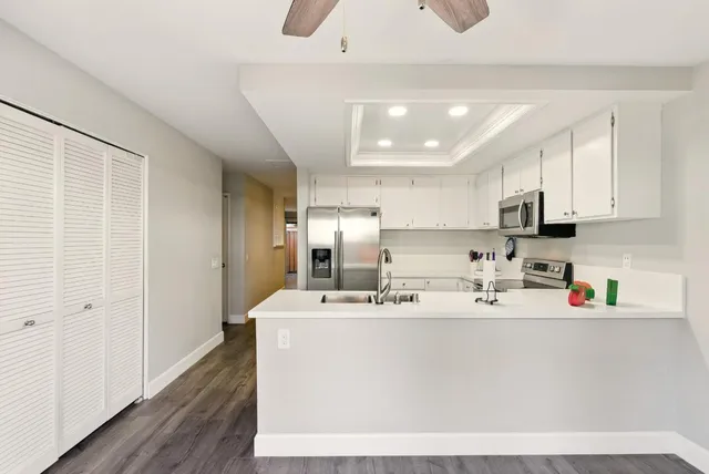 a white kitchen with stainless steel appliances granite countertop a sink dishwasher a refrigerator and white cabinets with wooden floor