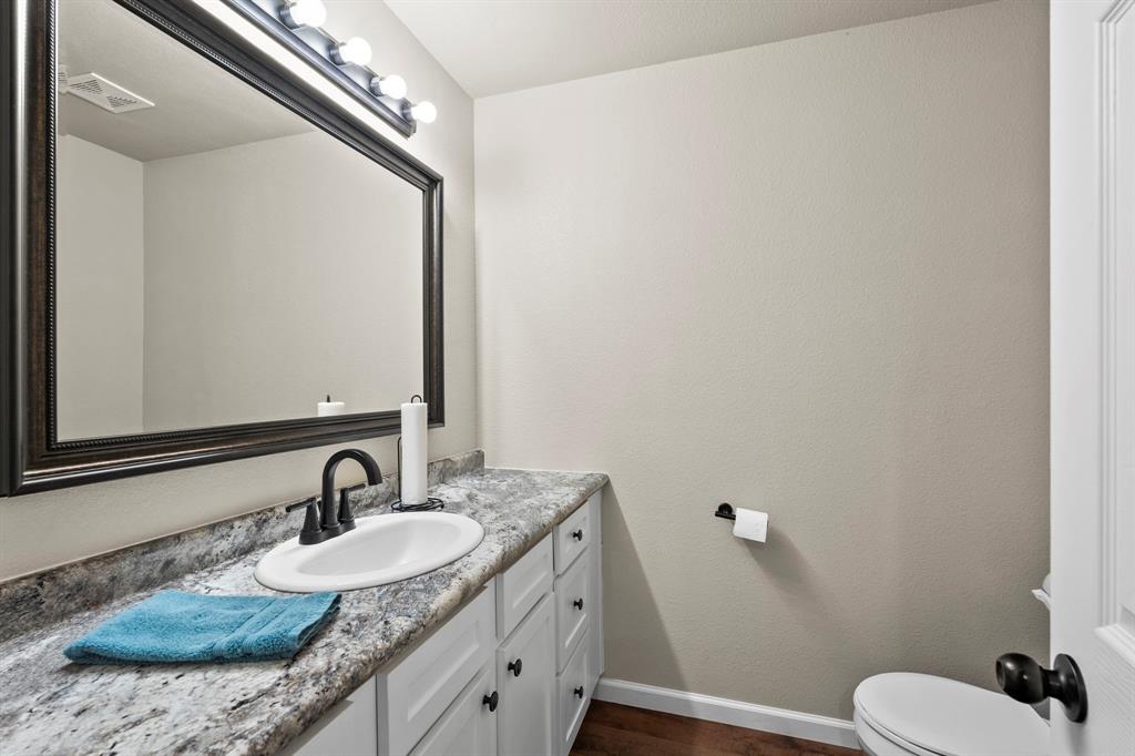 1404 McConnell Road Gunter, TX 75058 - Photo 17 of 27 a bathroom with a granite countertop sink a mirror and a toilet