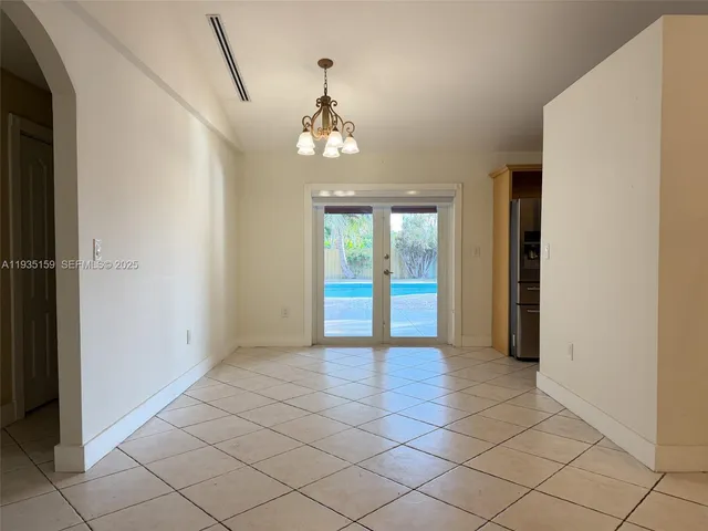 an empty room with kitchen view and a chandelier fan