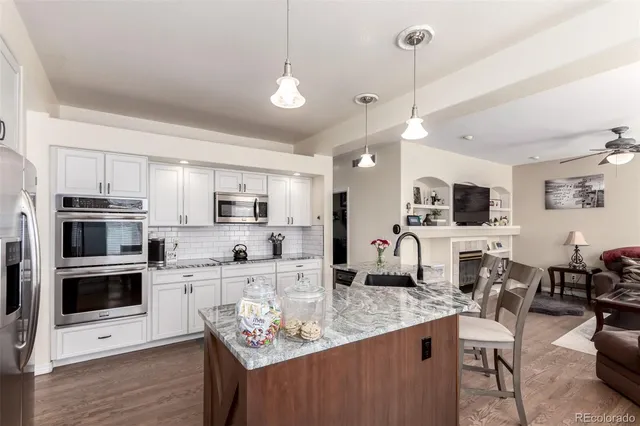 a kitchen with stainless steel appliances kitchen island granite countertop a stove top oven a sink a dining table and chairs with wooden floor