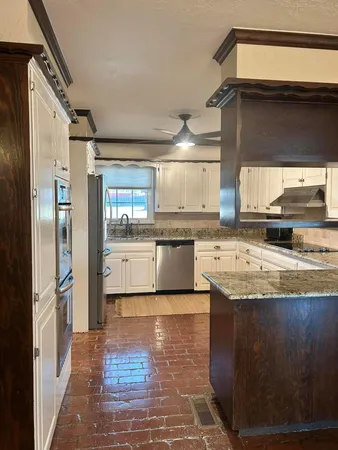 a kitchen with granite countertop a refrigerator a sink dishwasher a stove and white cabinets with wooden floor